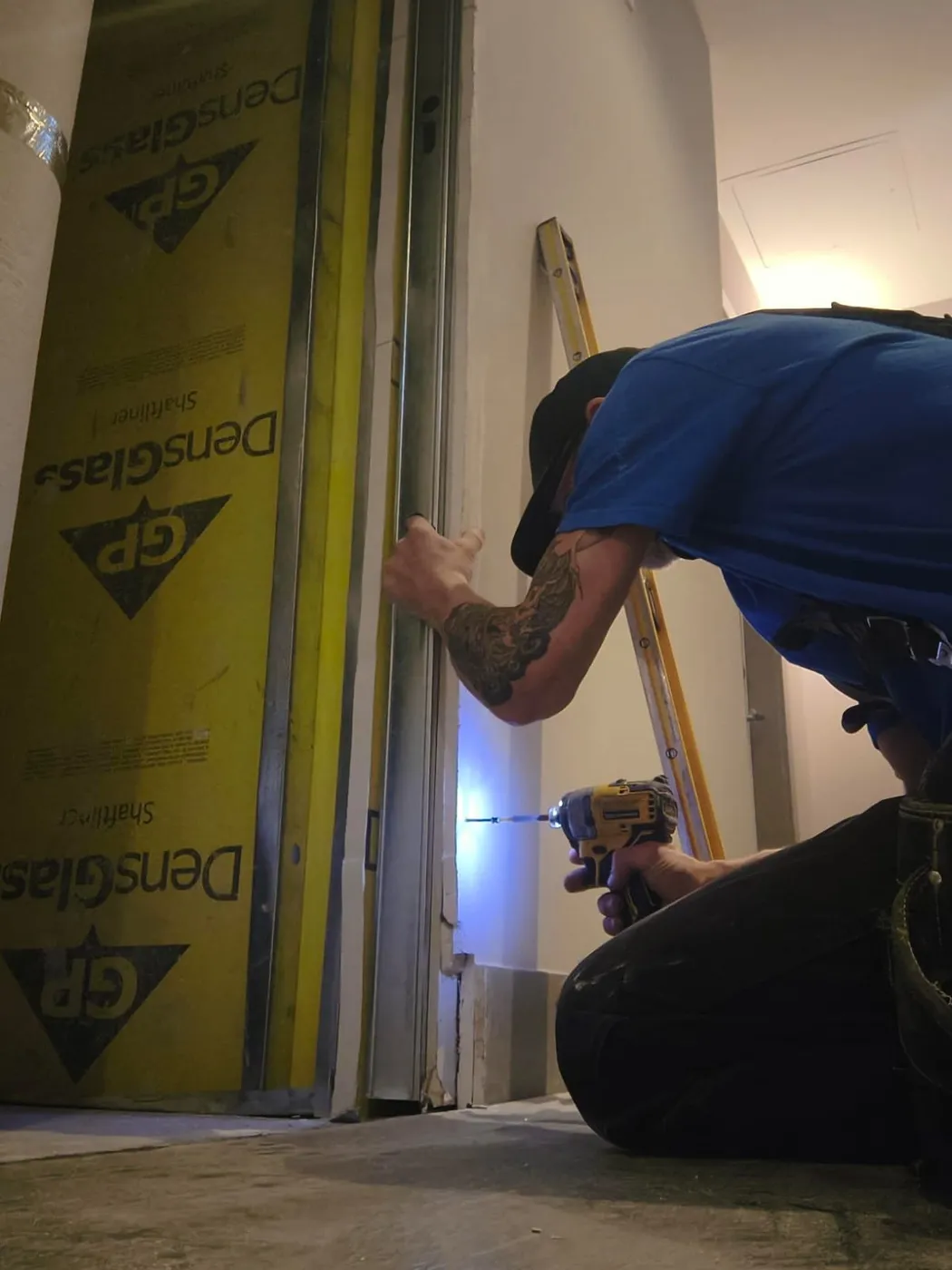 A Recap Group crew member kneeling to repair a wall frame with a drill